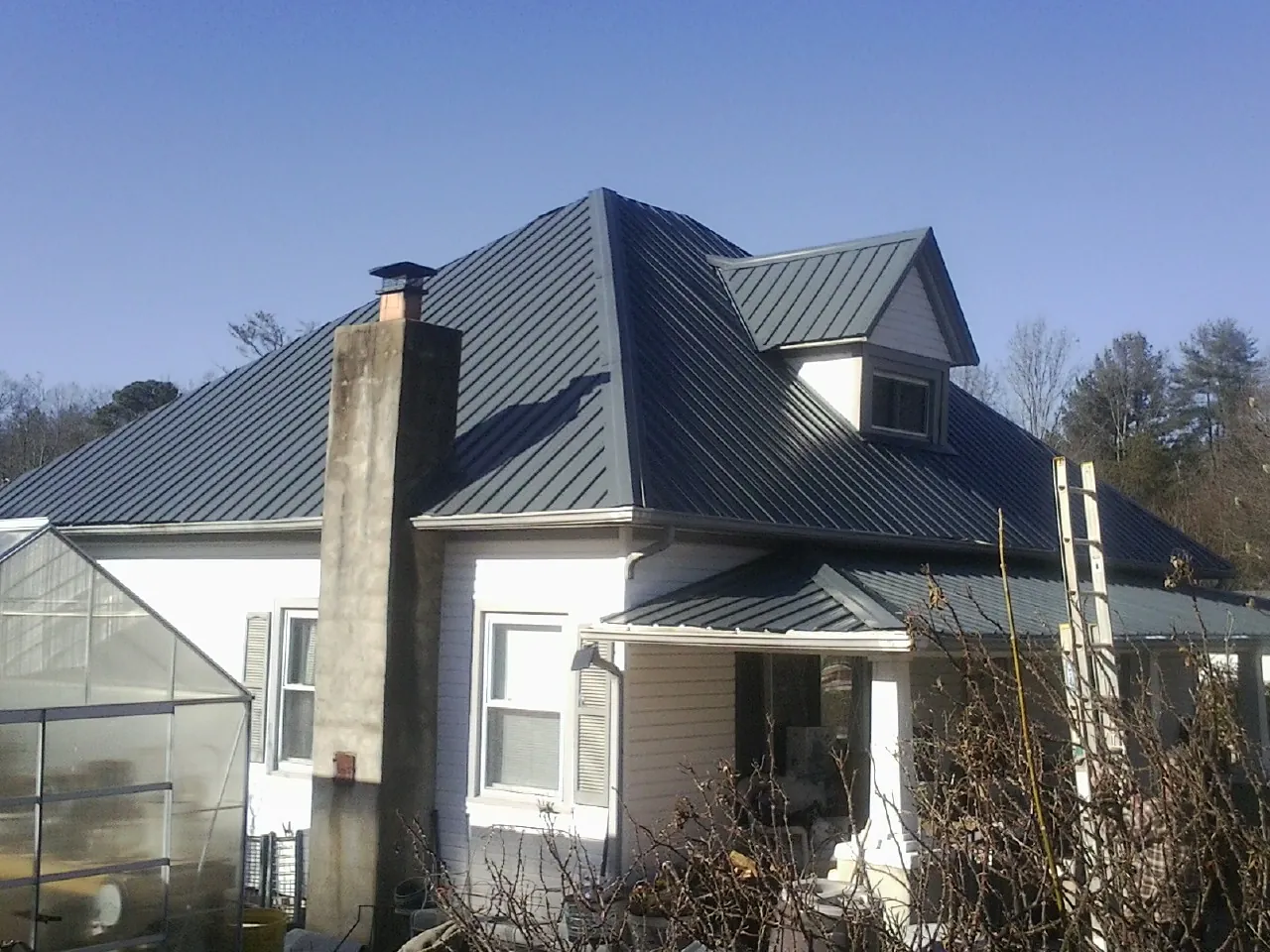 Dark blue standing seam metal roof on a white farmhouse with dormer — Slate & Tile Roof Repair by Roofing Brothers in Paxico