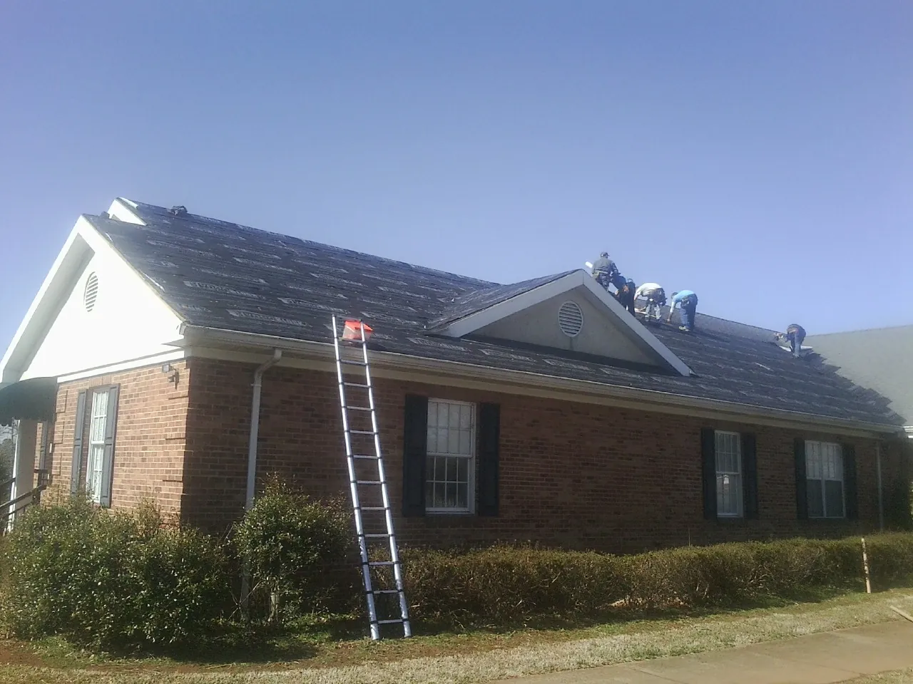 Crew tearing shingles off a brick ranch roof with a ladder set — Emergency Roof Repair work by our crew in Paxico