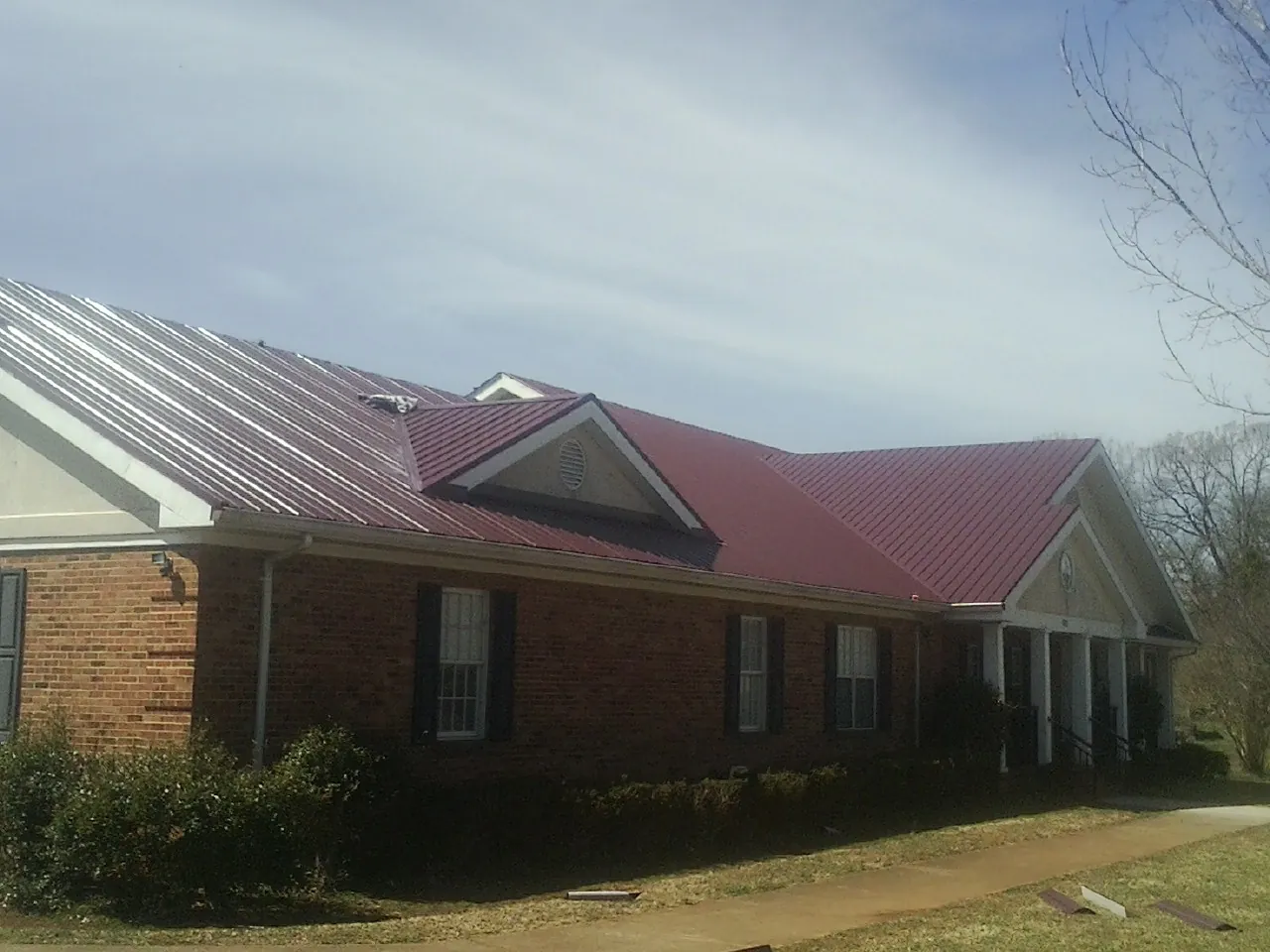 Red metal roof with gabled entries on a long brick building, from a Hail Damage Roof Repair job in Paxico