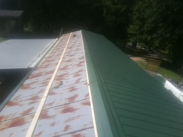 Old rusted panels beside newly installed green metal roofing — Wind Damage Roof Repair by Roofing Brothers in Paxico