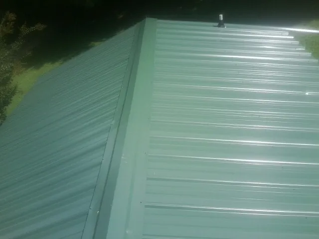 New green metal panels meeting at the ridge of a roof — Flat Roof Repair work by our crew in Paxico