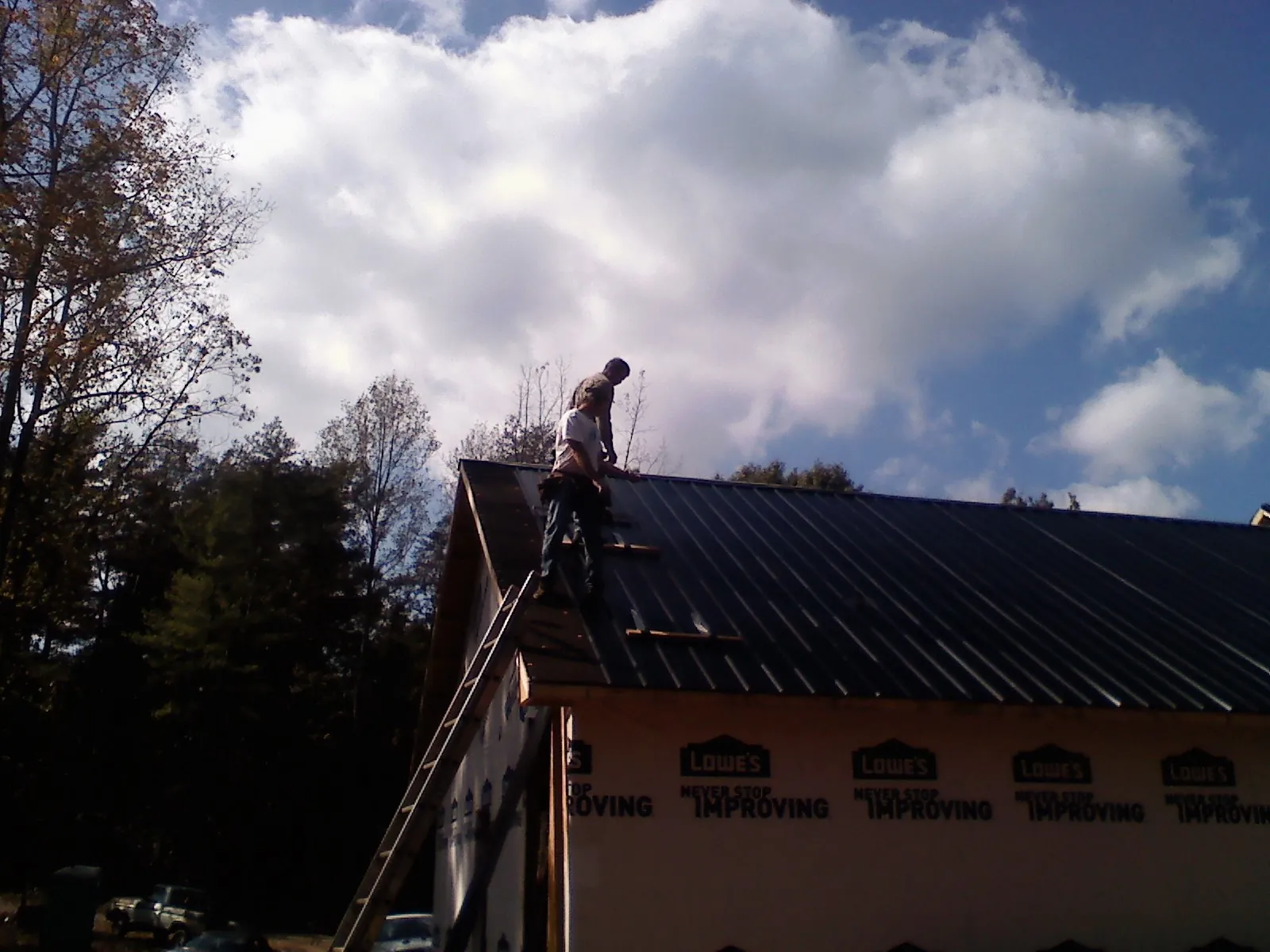 Roofer fastening dark metal panels high against a cloudy sky, from a Roof Inspection job in Paxico
