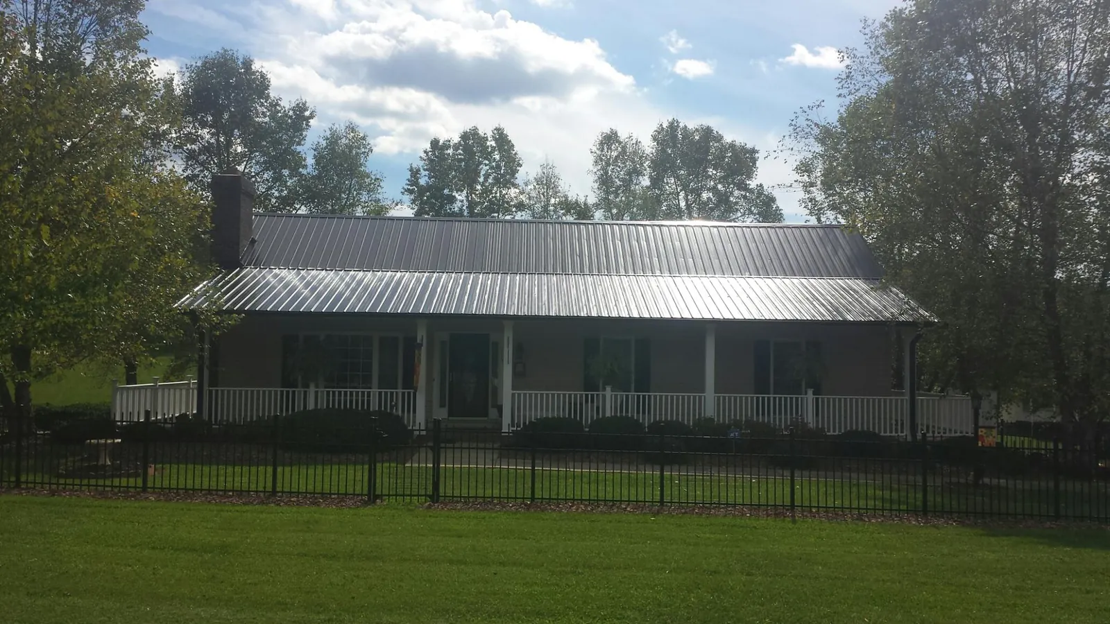 Gray metal roof on a brick ranch with a full width front porch — Gutter Guard Installation work by our crew in Paxico