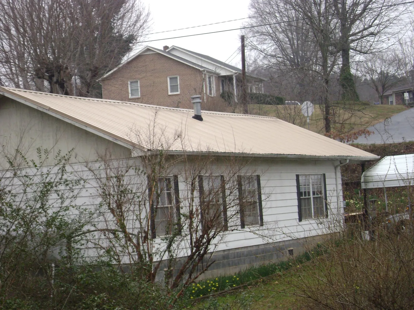 Tan metal roof on a white sided house set into a hillside — Commercial Roofing by Roofing Brothers in Paxico