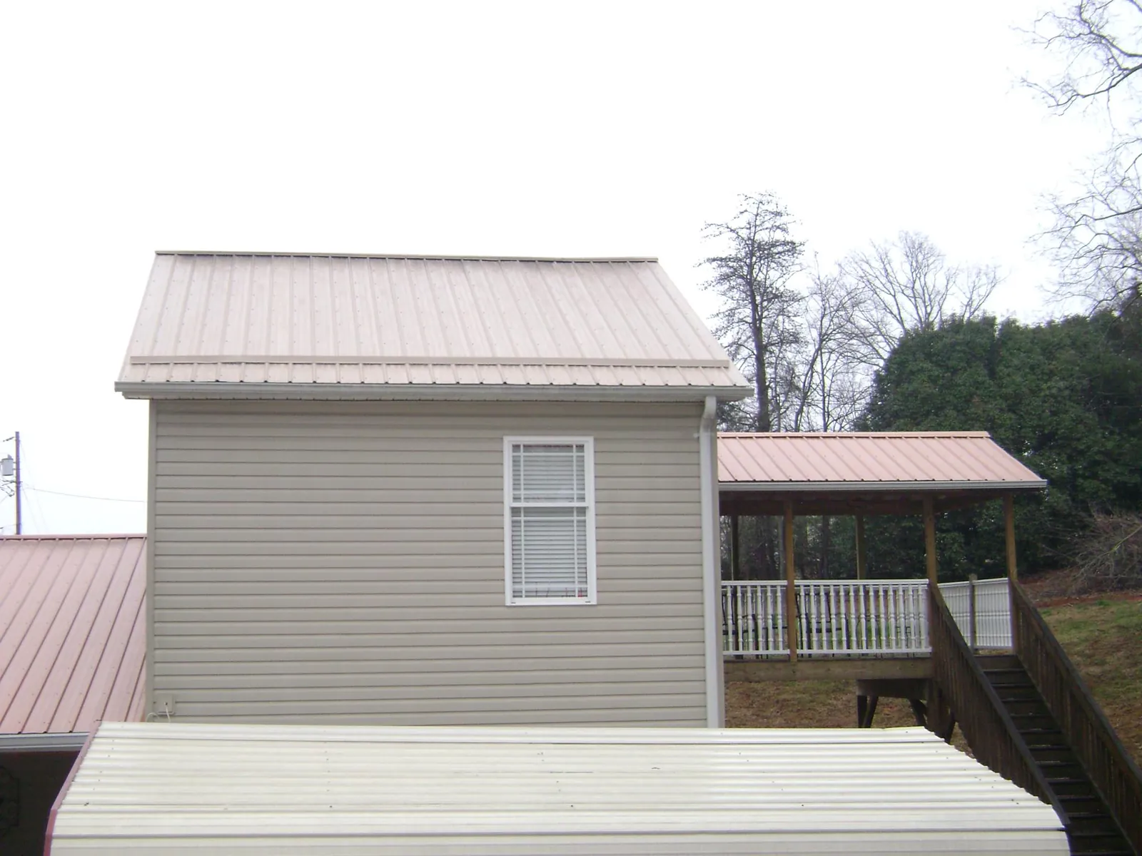 Tan metal roofs on a two story addition and attached porch, from a Roof Replacement job in Paxico